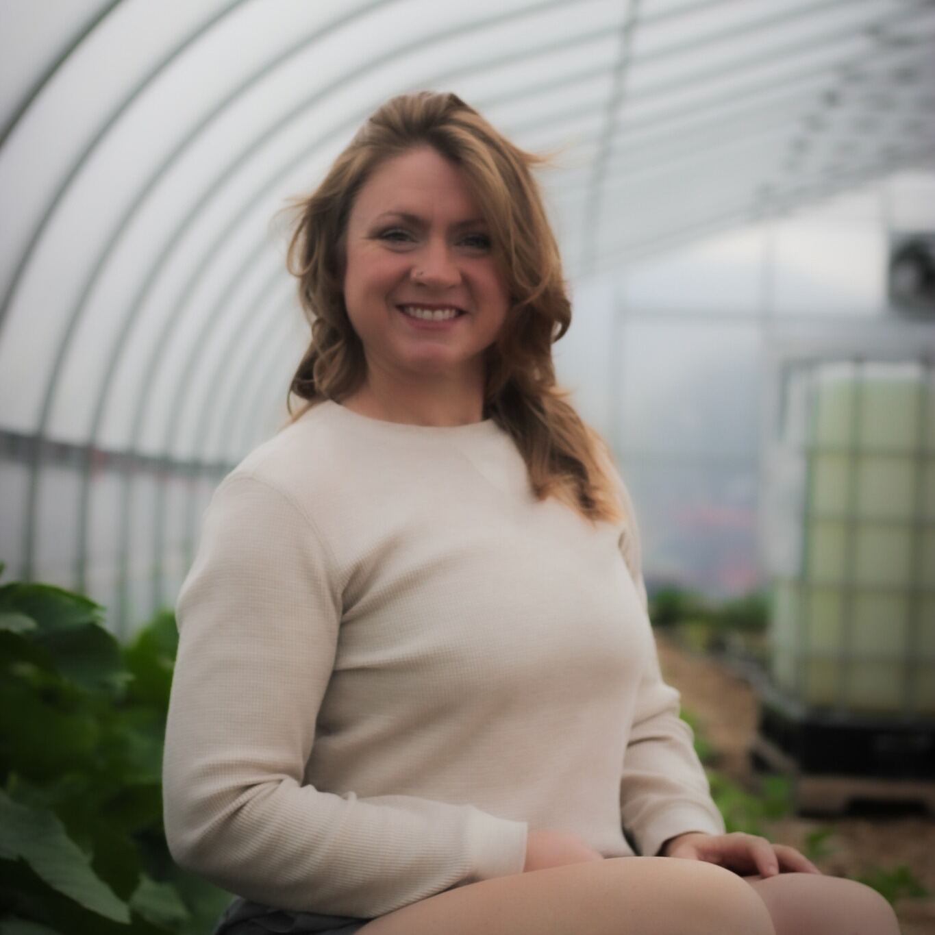 Smiling team member inside a sunlit hoop house