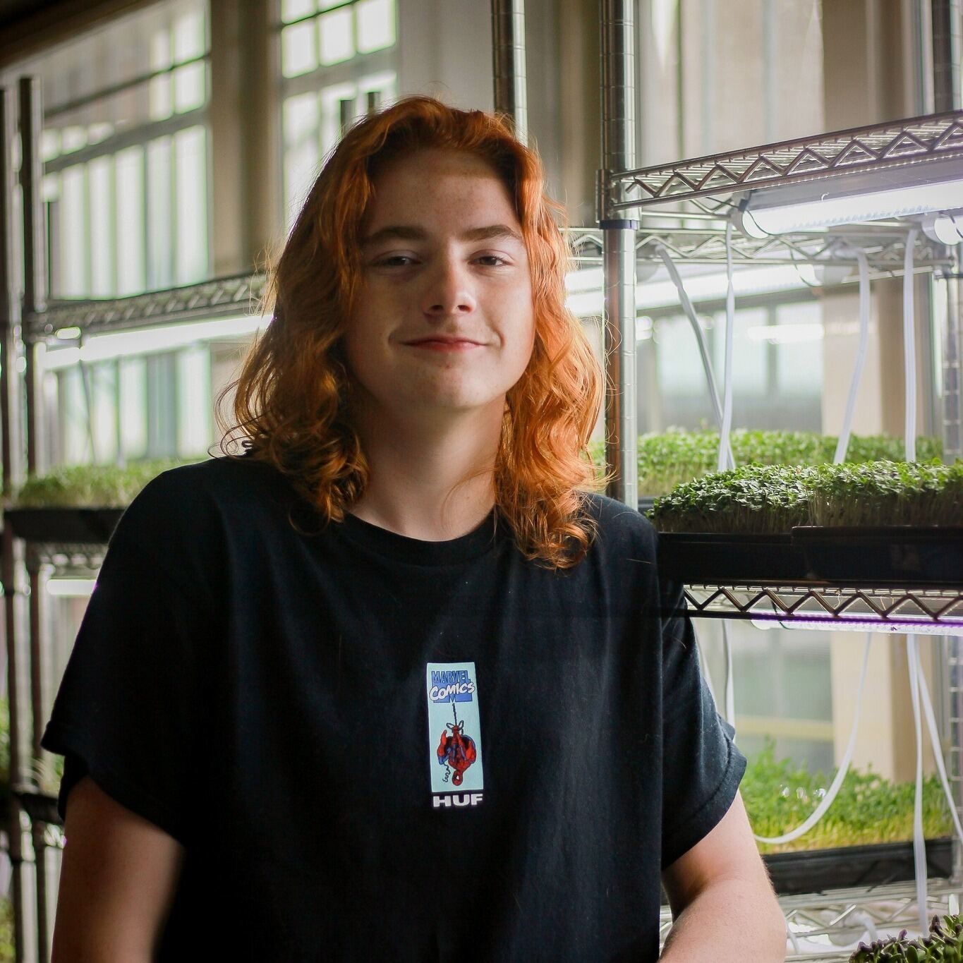 Young grower in front of trays of microgreens under grow lights